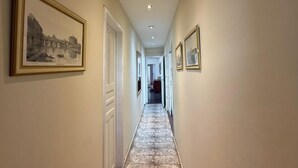 Un pasillo con cuadros en las paredes, piso de baldosas y una puerta al final.