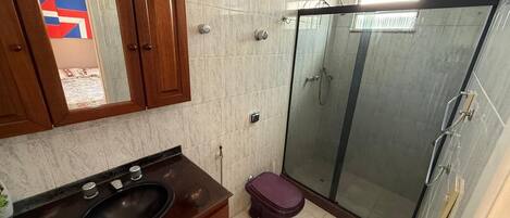 A bathroom with a glass shower enclosure, a wooden vanity with a sink, and a toilet.