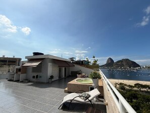 Una terraza en la azotea con piscina, zona de estar y vistas al océano y a una montaña.