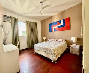 A bedroom with a bed, two bedside tables, a ceiling fan, a window with curtains, and a wall-mounted artwork. - PENTHOUSE BOTAFOGO Panoramic penthouse with large terrace in Rio de Janeiro (Rio de Janeiro)