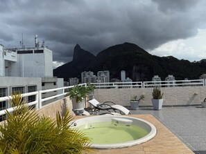 A rooftop terrace with a hot tub, lounge chairs, and potted plants.