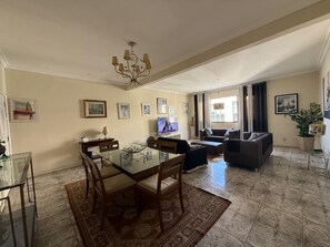 A spacious living area with a glass dining table, a sofa, and a television.