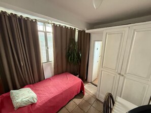 Una habitación con una cama, una planta en maceta, un armario blanco y una puerta que da a otra habitación.