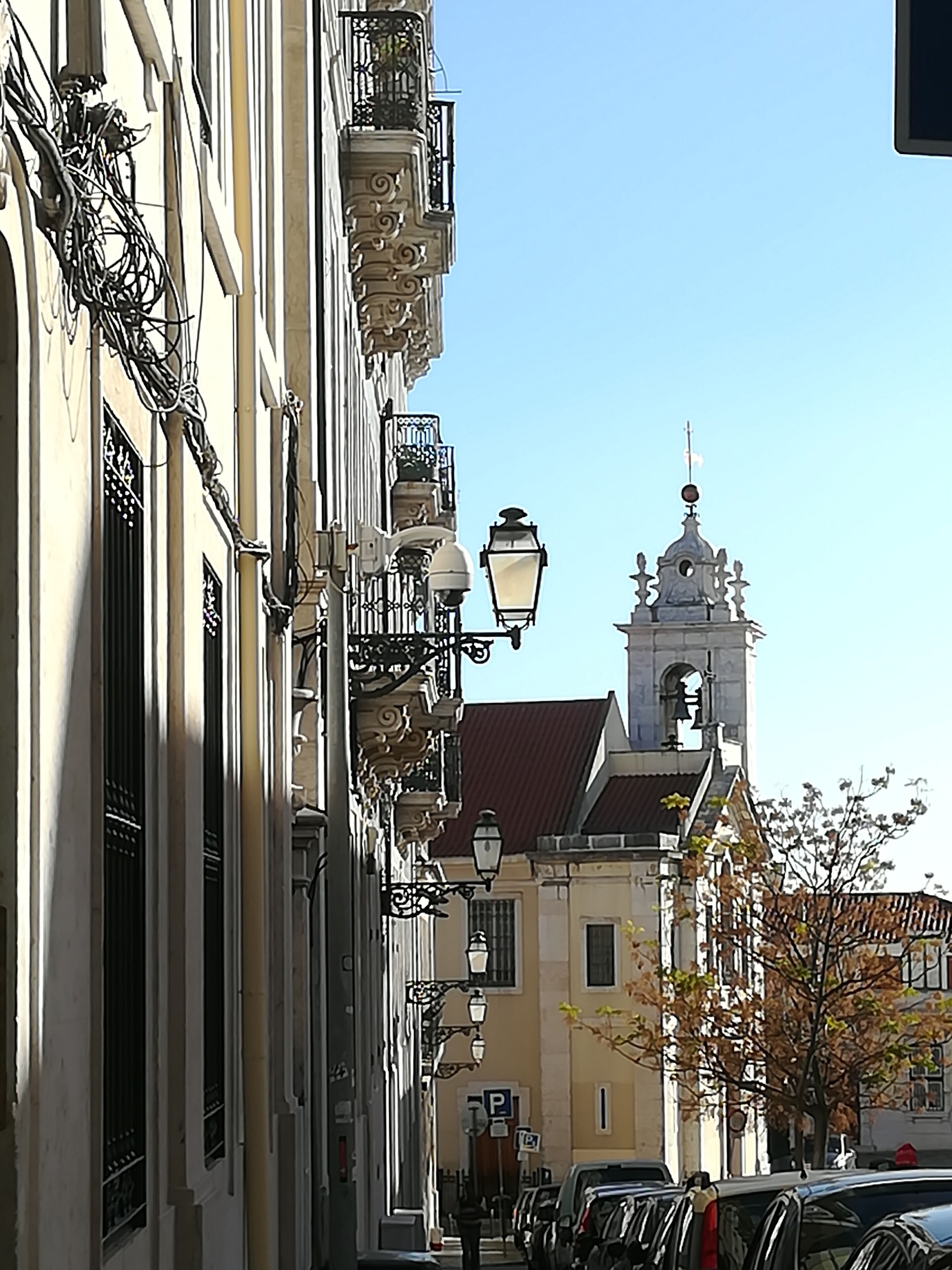 A street with historic buildings, a church tower, and parked cars.