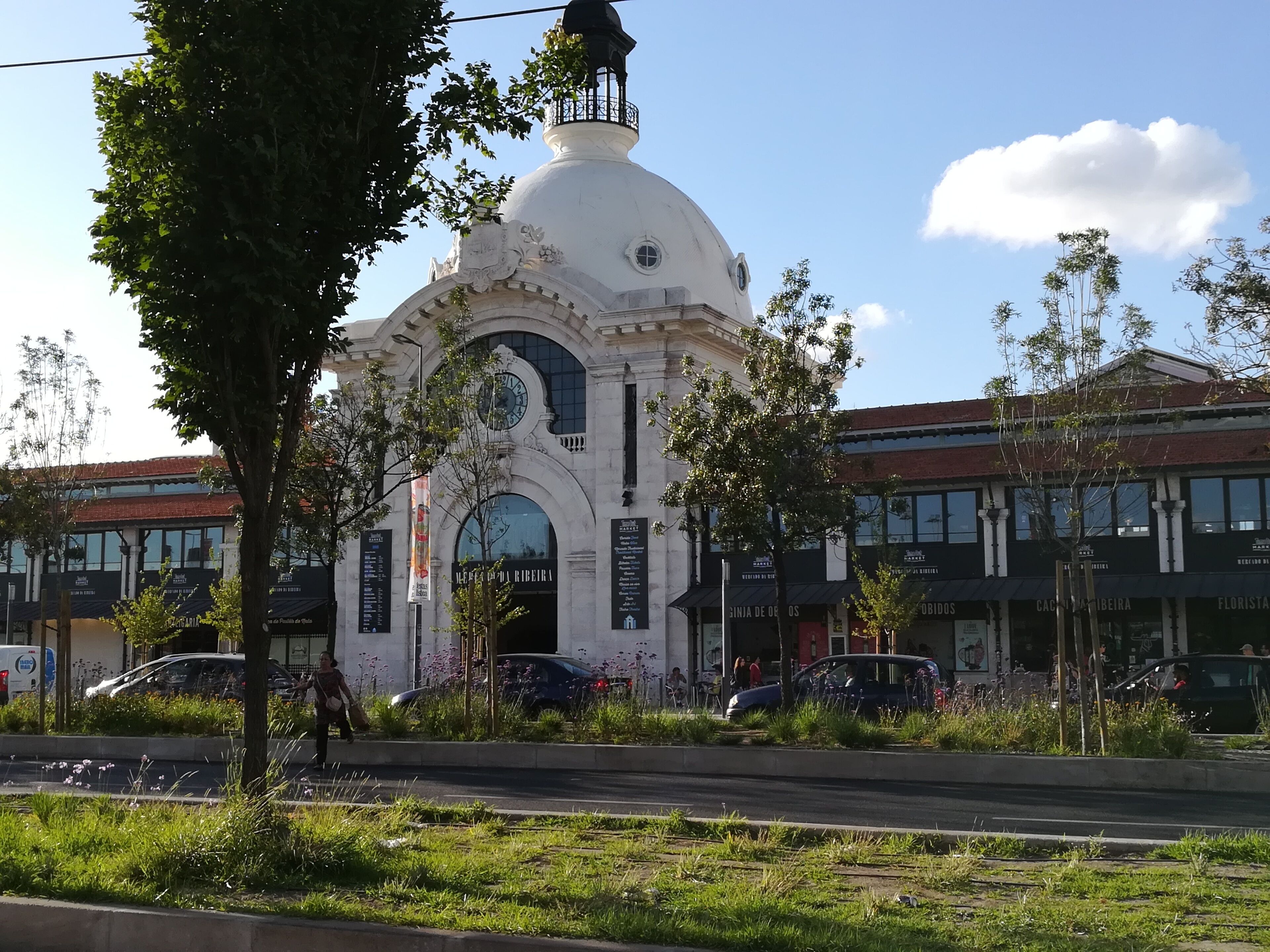 En vit byggnad med en kupol och välvda fönster, omgiven av grönska och moderna byggnader.