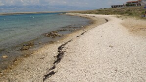 Une plage de galets qui mène à une étendue d’eau calme, avec un bâtiment visible au loin.