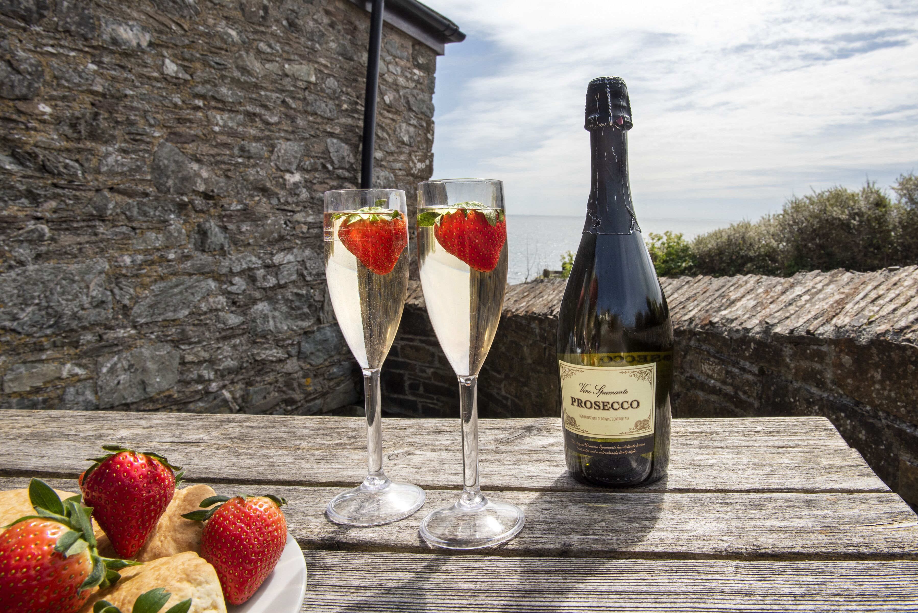 Two glasses of a white beverage with strawberries, a bottle of Prosecco, and strawberries on a wooden table.