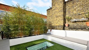 A modern outdoor seating area with a glass-top table and a green lawn.