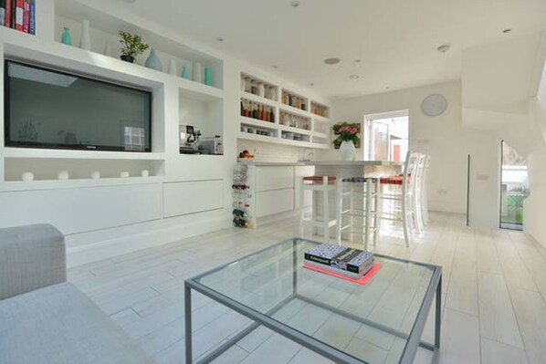 Une cuisine moderne avec des meubles blancs, une table basse en verre et un coin repas avec des chaises.
