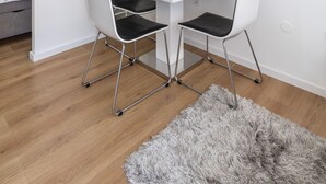 Een moderne kamer met een glazen eettafel, twee stoelen, een zacht vloerkleed, een klok, een raam met ruitverdeling en een Picasso schilderij.