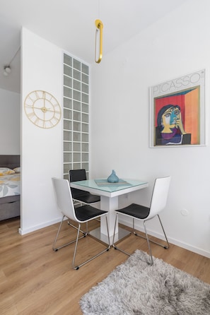 A modern room with a glass dining table, two chairs, a fluffy rug, a clock, a window with a grid pattern, and a Picasso painting.