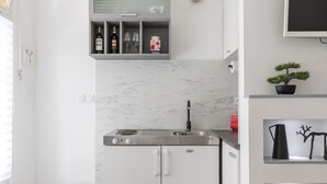Een moderne keuken met een ingebouwde kookplaat, spoelbak en witte kasten. Daarboven bevindt zich een klein plankje met decoratieve objecten en een potplant.