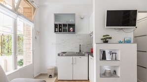Een kleine keuken met een inbouwoven, een magnetron en een spoelbak. Er hangt een televisie aan de muur boven het aanrecht.