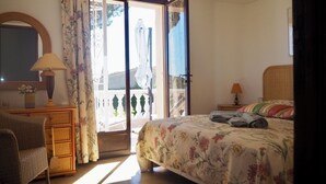 A bedroom with a bed, a chair, a dresser, a lamp, and a window with curtains. - Gorgeous sea view, heated pool, jacuzzi, sauna, close to the beach. (Sainte-Maxime)