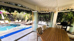 Un espacio al aire libre cubierto con piscina, sillas de descanso y una mesa con sillas.
