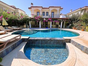A swimming pool with a sun terrace, lounge chairs, and a building with a balcony in the background.