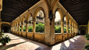 Un patio interior con una serie de arcos y columnas, piso de baldosas y vista de un edificio al fondo.