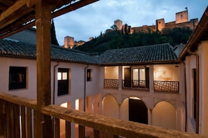 A courtyard with a wooden railing, arched doorways, and a view of a castle in the background. - Casa del Beso (Granada)