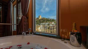 Un baño con bañera, una ventana que ofrece vistas a un castillo y una botella de champán.