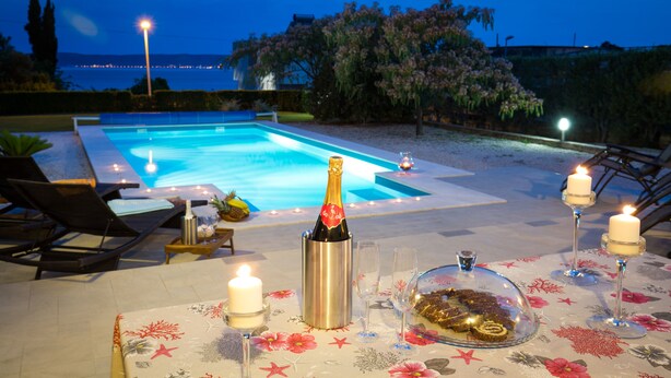 An outdoor pool area with lounge chairs, candles, and a bottle of champagne on a floral tablecloth. -  Luxury villa with private heated pool, hot tub,  mini golf,  spacious inter... (Kaštel Kambelovac)