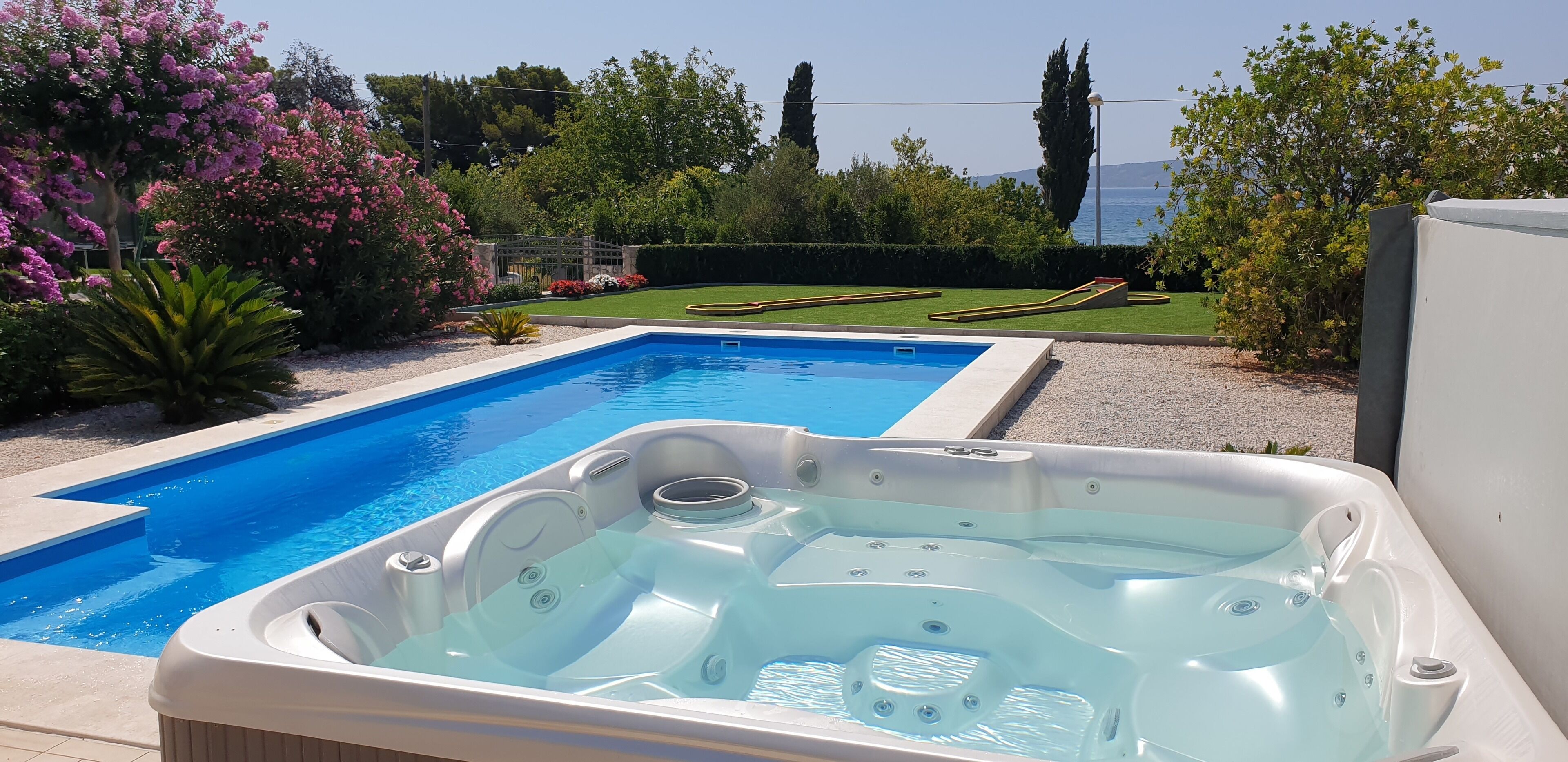 En swimmingpool med et boblebad, omgivet af frodig vegetation og en uhindret havudsigt.