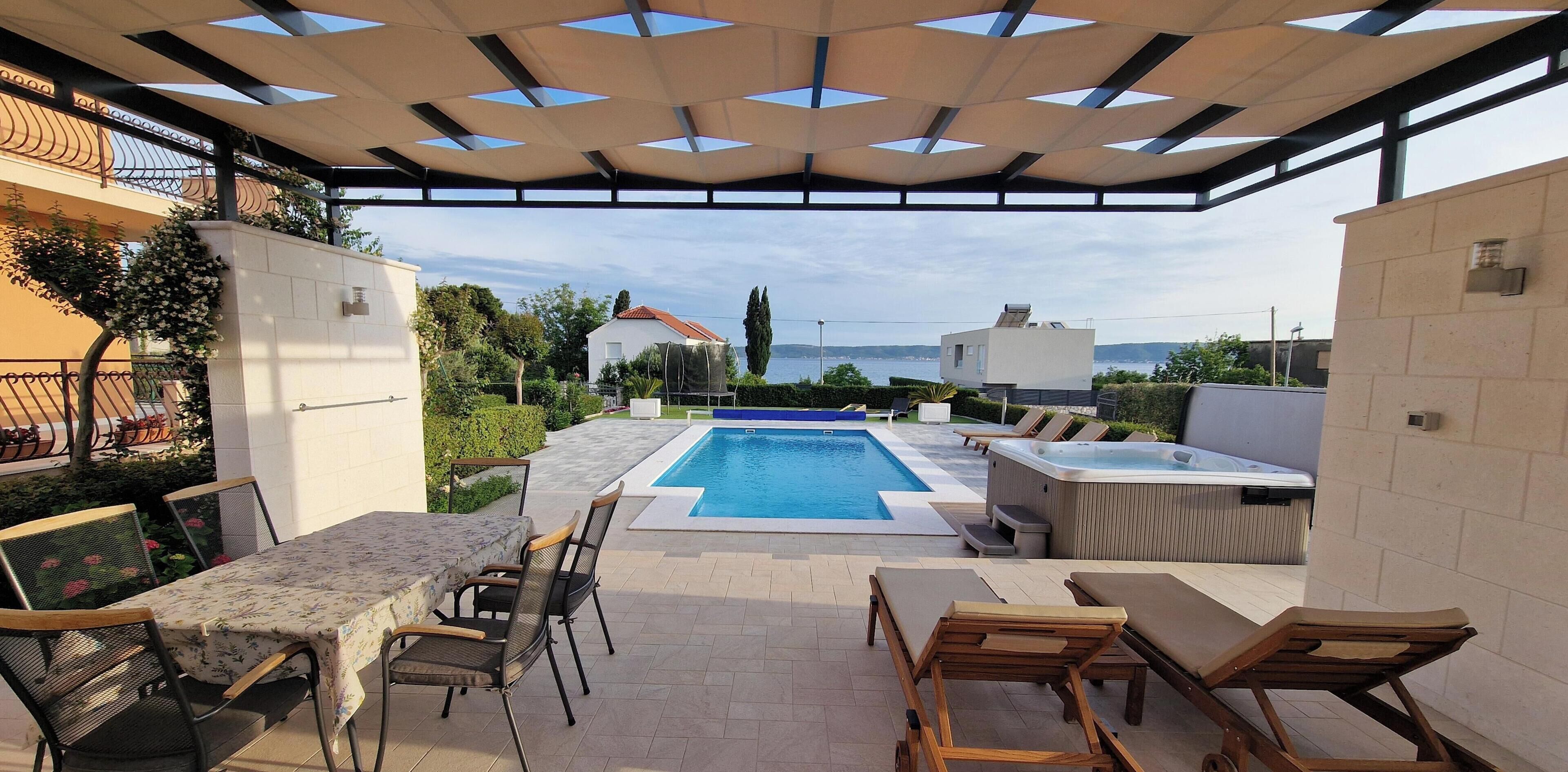 Ein überdachter Außenbereich mit Pool, Liegestühlen und Whirlpool.