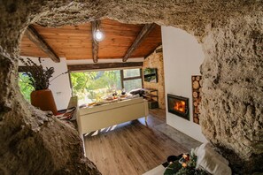Un interior rústico con pared de piedra, techo de madera, cama, chimenea y ventana con vistas al follaje.