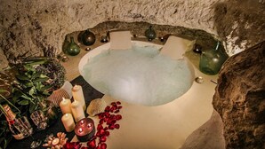 A spa bath with candles, rose petals, and decorative vases. - Cave Suite GUHA (Cave Hotel Lomas de Ruvira) (Jorquera)