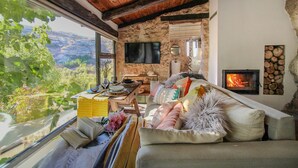 A cozy living room with a stone fireplace, a television, and a view of the outdoors. - Cave Suite GUHA (Cave Hotel Lomas de Ruvira) (Jorquera)