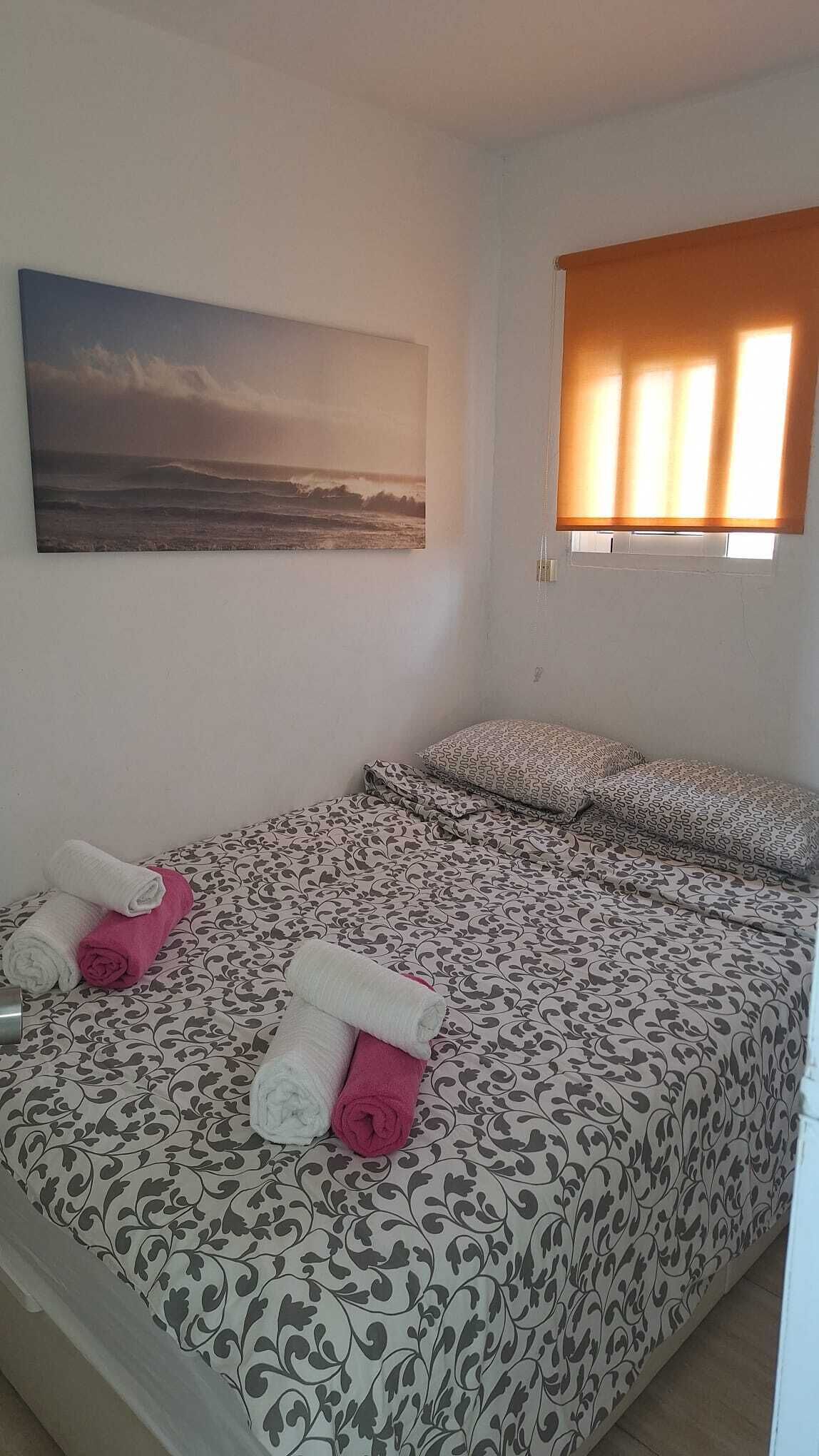 Une chambre à coucher avec un lit, des oreillers, un tableau et une fenêtre avec des stores.