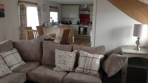 A living room with a striped sofa, a fireplace, and a kitchen in the background. - Beautiful Country Cottage Pet Friendly  Sleeps 7 Near Cardiff (Cardiff)
