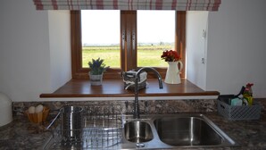 A kitchen with a double sink, a window with a view of a field, and a potted plant on the windowsill. - Beautiful Country Cottage Pet Friendly  Sleeps 7 Near Cardiff (Cardiff)