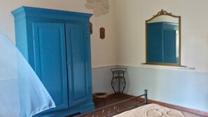 Een kamer met een grote blauwe garderobe, een klein tafeltje met kandelaar en een spiegel aan de muur.