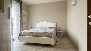 A bedroom with a white bed, a bedside table with a lamp, and a window with sheer curtains. - The Seagull apartment Sirmione | Spa & Garda Lake (Sirmione)