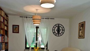 A living room with a sofa, a table with flowers, a bookshelf, and a large wall clock.