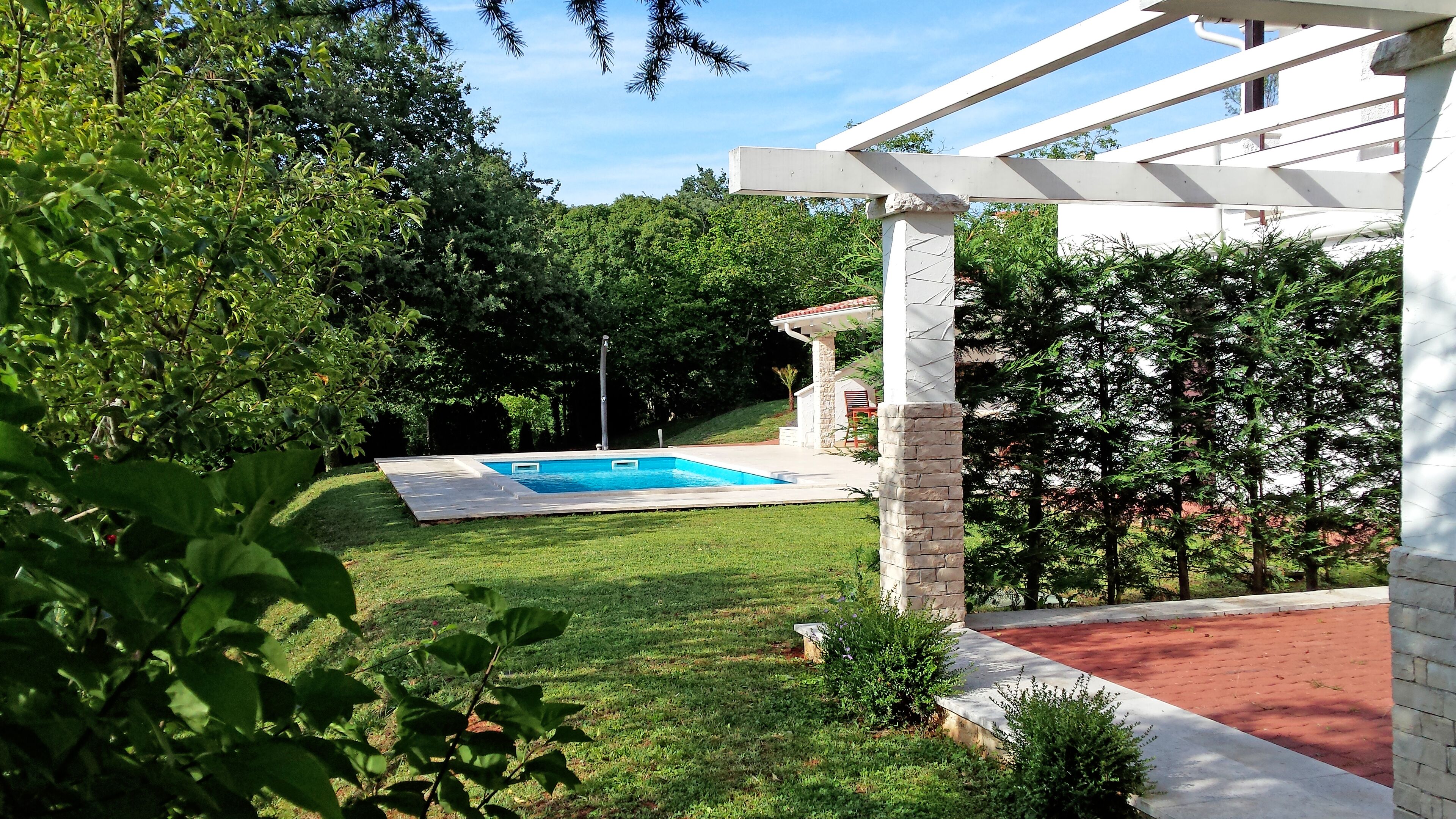 A backyard with a swimming pool, a pergola, and a stone pillar.