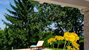 A poolside table with a croissant, two glasses of orange juice, and a vase of yellow flowers.