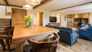 A spacious living room with a wooden dining table, blue sofas, and a television. - Atherstone Farm Cottage - charming thatched cottage, sleeps 4 guests in 2 rooms (Ilminster)