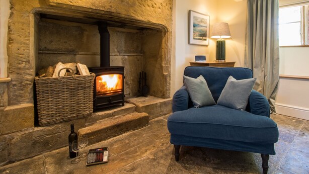 A cozy living room with a stone fireplace, a blue armchair, and a small table with a lamp. - Atherstone Farm Cottage - charming thatched cottage, sleeps 4 guests in 2 rooms (Ilminster)