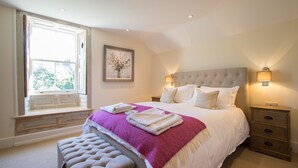 A bedroom with a large bed, a window seat, a nightstand, and a wall-mounted lamp. - Atherstone Farm Cottage - charming thatched cottage, sleeps 4 guests in 2 rooms (Ilminster)