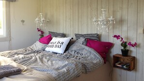 Un dormitorio con cama, almohadas, una araña y un estante pequeño con libros.