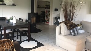 Una sala de estar con sofá, una mesa de comedor con sillas, una chimenea negra y una estantería llena de libros.