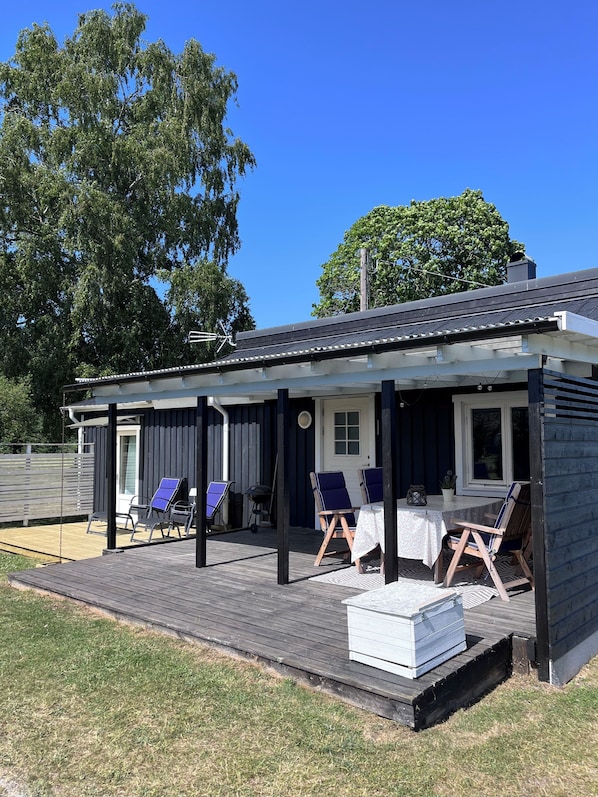 A wooden deck with outdoor seating, a covered area, and a building with a dark exterior and white trim. - Houses on the gorgeous island of Gotland (Dalhem, gotland)