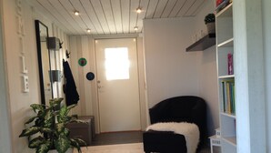 Una sala de estar moderna con piso de madera, un sofá negro con una manta blanca, una estantería y una planta en maceta.
