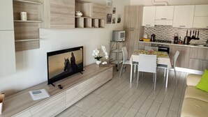 A modern living room with a flat-screen TV, a dining area with a table and chairs, and a kitchen with cabinets and appliances. - Delightful apartment with beautiful lake view (Desenzano del Garda)