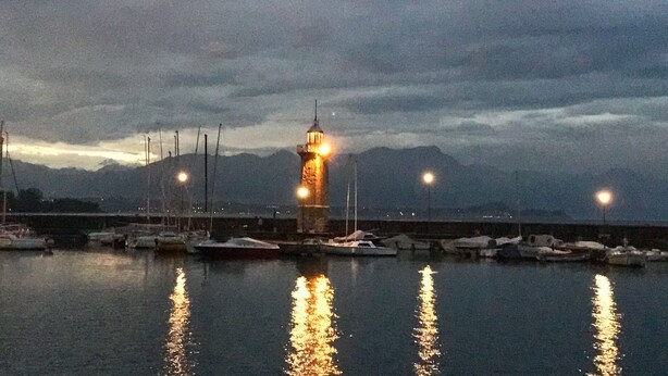 A harbor with boats docked, a lighthouse, and mountains in the background. - Delightful apartment with beautiful lake view (Desenzano del Garda)