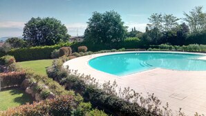 A curved swimming pool surrounded by lush greenery and a clear blue sky. - Delightful apartment with beautiful lake view (Desenzano del Garda)