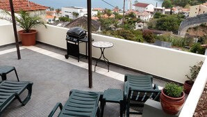 A terrace with outdoor furniture, a grill, and a view of the sea and buildings. - Vivenda Linda Vista 2  Spectacular sea and mountain views in Porto da Cruz (Porto Da Cruz)
