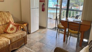 A living room with a sofa, a dining table with chairs, a white refrigerator, and a television mounted on the wall. - Vivenda Linda Vista 2  Spectacular sea and mountain views in Porto da Cruz (Porto Da Cruz)