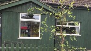 A green wooden building with a white window and a hanging flower pot. - PLAN YOUR ISLAND ESCAPE TO THE BEAUTIFUL SCOTTISH ISLE OF CUMBRAE (Millport)